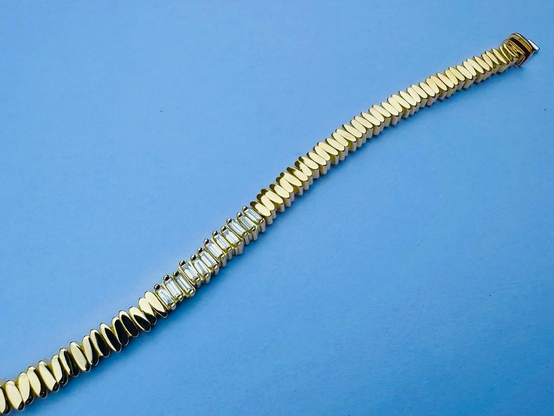 A gold bracelet made of rice grain components and set with baguette shaped diamonds is laying on a blue background
