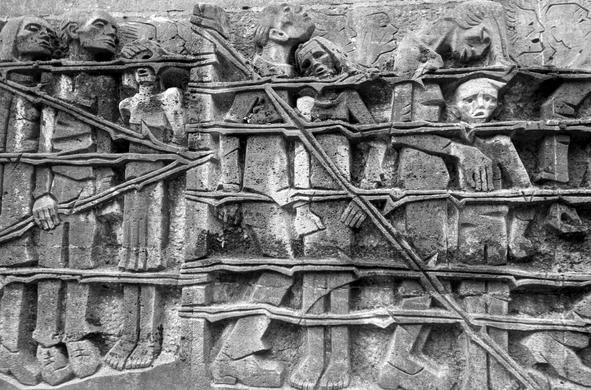 A monochrome photograph depicting a wall filled with statues, honoring the memory of those murdered in Dortmund during Easter 1945.

Eine Schwarzweissfotografie, die eine mit Statuen gefuellte Wand zeigt, die an die Ermordeten von Ostern 1945 in Dortmund erinnert.