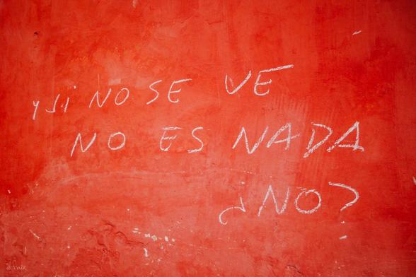 Texte en espagnol à la craie sur un mur badigeonné rouge. Sa traduction : "Et si ça se voit pas, ça n'existe pas. Non ?"