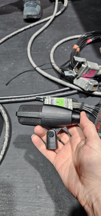 A stupid white hand holds a prototype Sennheiser MD421 mini microphone! It's about half the length of a normal 421 (about 3 inches) and has a standard microphone stand mount rather than the horrible slide clip from the regular 421. A spaghetti of cabling can be seen on the stage floor in the background.