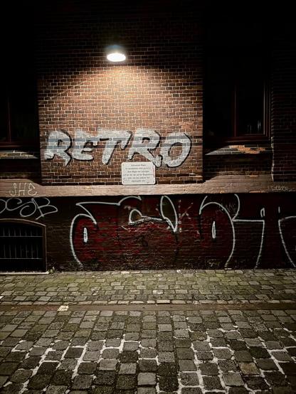 Fassade im Dunklen mit Scheinwerfer beleuchtet und dem Spruch „Retro“ auf Backstein