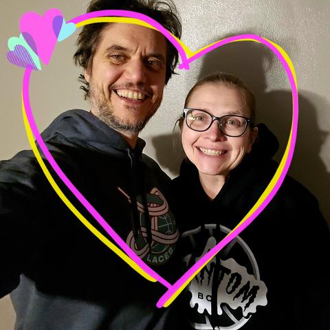 Selfie of a couple with a heart drawn around them. They each wear a hooded sweatshirt. One is grey and has the Laces BC logo on it. The other is black and has the Phantom BC logo on it.
