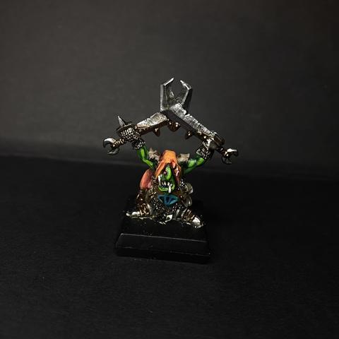 A heavily armoured goblin with two swords, and an orange hood covering part of its face. Its gut bears a blue eye.