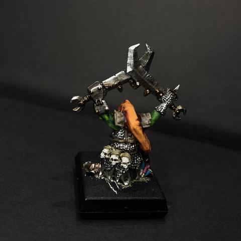 Rear of a heavily armoured Goblin. They have two grubby swords lifted above theirs head and a long hanging hood. Colourful mushrooms grow from the space beside its foot