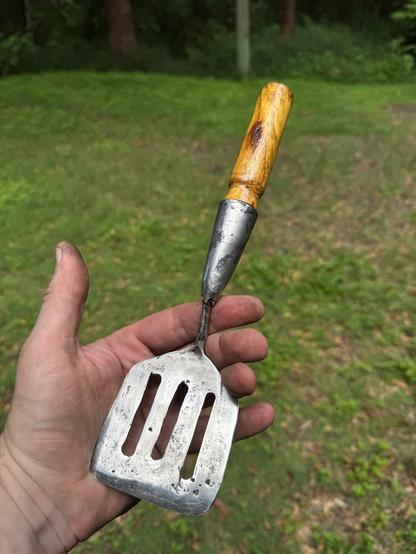 Finished egg-flip with cone ferule and wooden handle inserted. Front view. 

The flipper end is about as big as my palm, the cone is welded on at the point of the bend in the original shank.
