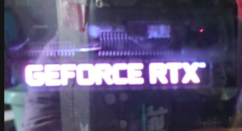 Photograph of the side of a tower computer showing the lit up notce GEFORCE RTX from the GPU which is plugged into the motherboard. The side of the computer is partly mirrored and shows a slight image of the person taking the photo (me)