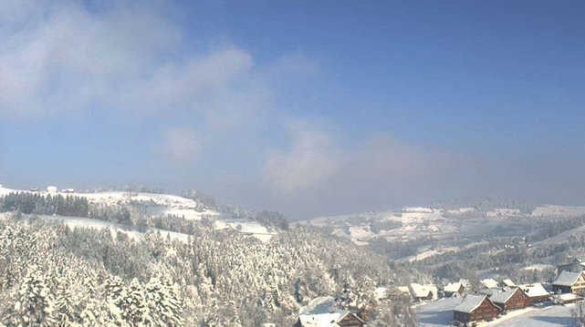 Verschneite Hügel mit Häusern und blauem Himmel darüber. Die Sonne scheint.