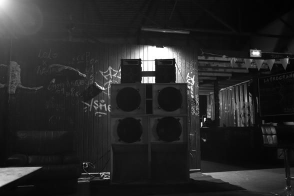 Photo en noir et blanc prise dans l'entrée de la salle de concerts Grrrnd Zero (à Lyon En Velin) le 13 février 2025. On y voit deux énorme enceintes et des parois métalliques. Ce jour là Sürya, Boucan et Traum ont joué sur la scène de Grrrnd zero.