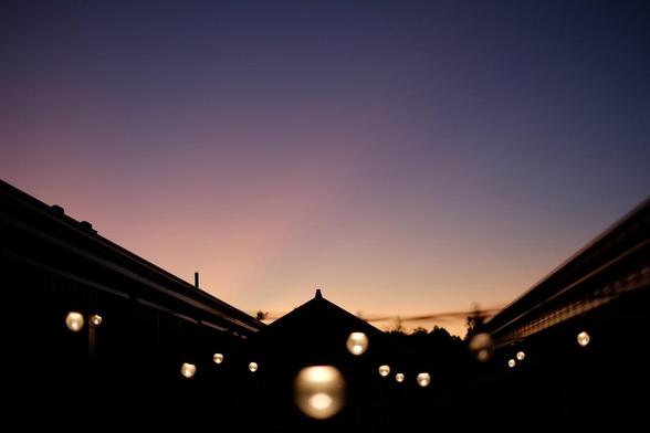 A silhouette of a rooftop with string lights against a colorful sunset sky, featuring shades of pink, purple, and orange.