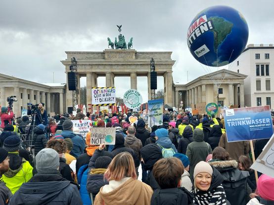 Blick aufs Brandenburger Tor, davor viele Menschen mit Plakaten, in Winterkleidung auf dem Pariser Platz. Rechts schwebt die Erde als Ballon mit der Aufschrift: Klima retten! vom BUND