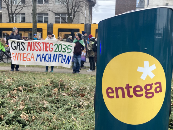 Hinter einer Stromladesäule des Darmstädter Energieversorgers Entega haben sich Demonstrierende mit einem Banner mit der Aufschrift „Gasausstieg 2035 - Entega mach n Plan“ postiert.