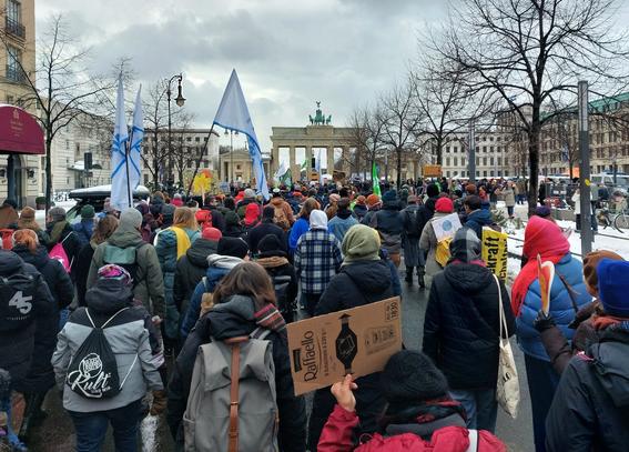Der Demozug zueht Richtung Brandenburger Tor, das im Hintergrund zu sehen ist. Im Vordergrund die Rückseite eine Pappschilds - offenbar von einem Karton voller Raffaello.
