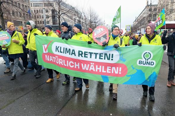Sechs Menschen vom BUND halten ein Banner mit der Aufschrift "Klima retten - Natürlich wählen". Im Hintergrund weitere Demonstrierende.