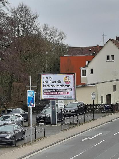 auf einem Parkplatz ein Großflächenplakat mit der Aufschrift "Hier ist kein Platz für Rechtsextremismus".