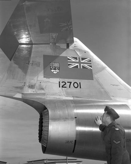An RCAF pilot gazes up at the tail of a CF-104 recently delivered to the RCAF at Cold Lake, Alberta, 1962. It features a large Red Ensign and the tail number 12701.