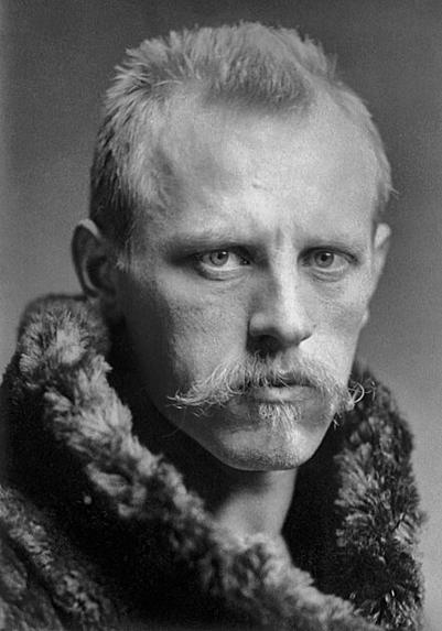Black and white portrait of a rugged blond man with a large mustache and fur coat stares into the camera.
Fridtjof Nansen