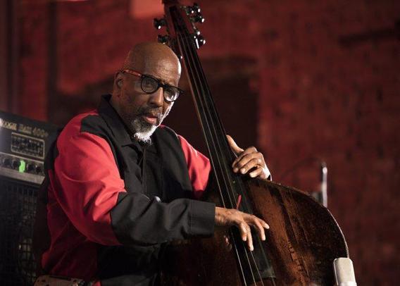 A goatee'd, bespectacled black man (William Parker) holds an upright bass and peers in the direction of the photographer.