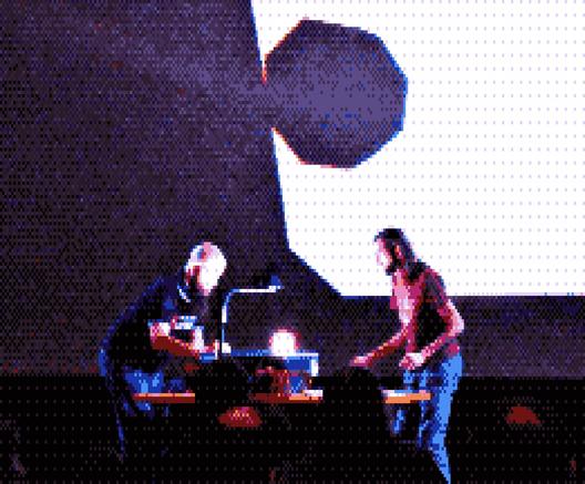 Photo of two people doing an overhead projector show, a glowing object in the center