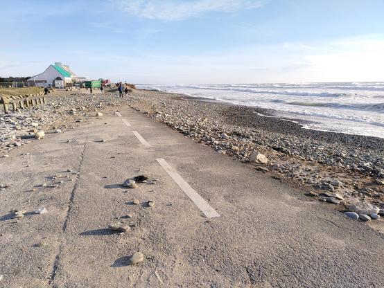 Route littorale parsemée  de galets projetés par l'océan à droite.