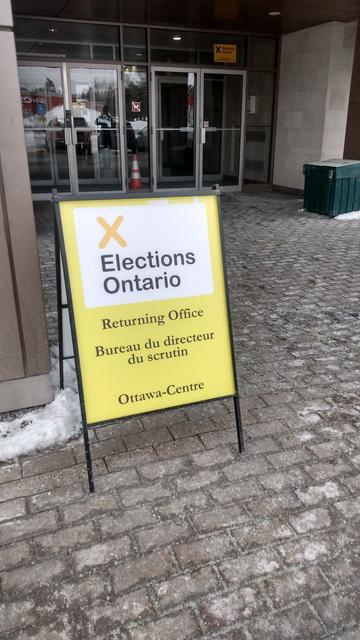 Yellow sandwich board in front of office entrance "elections Ontario returning office, bureau du directeur du scrutiny, Ottawa-Centre".
