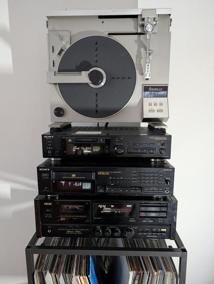 good looking HiFi components stacked on top of each other according to the content description. Below is a rack with records visible in front of a white wall