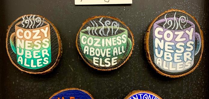 Three hand-painted wood cookie magnets. The first and last feature a steaming coffee mug painted in different soothing colors, with the phrase “COZY NESS UBER ALLES” painted on the mug in four lines. The reason is that I could only fit 4-5 letters across and thought it would look weird if the first line said “COZI” so I made the creative decision to yet have it all spell out to “Cozyness.”  Then the second one is a tea cup instead of a mug, so “Coziness” fit all the way across the top, with “above all” underneath and “else” at the bottom.