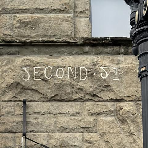 Lettering of unknown age adorns an old brick building. The sign reads “Second St.” but instead of using the letter S, both words begin with an upside down and horizontally flipped number 2.