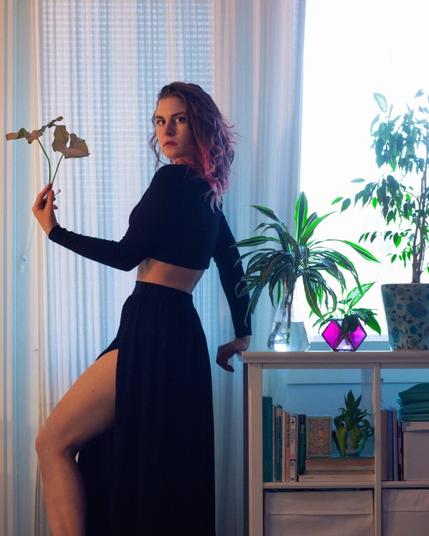 a woman in black crop top and split skirt posing with house plants