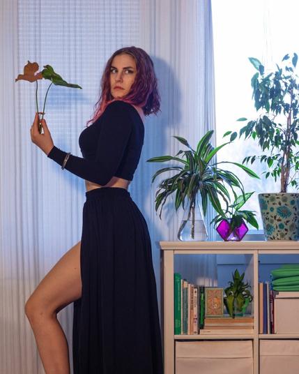 a woman in black crop top and split skirt posing with house plants
