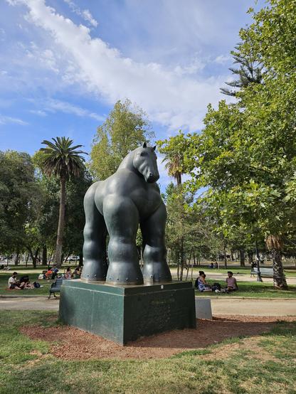 Green statue of a really muscular horse on a pedestal in a public park