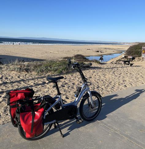 Sunday, February 9, 2025
Seaside Beach, part of California’s Monterey State Beach

A silver-blue Tern NBD P8i with red panniers is facing north.  Across the Monterey Bay waters, the Santa Cruz mountains are visible.