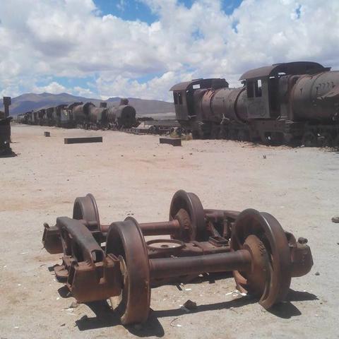 Photo of a frame with train wheels, at the back there are abandoned and rusted wagons and locomotives