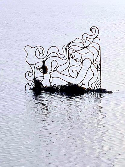 A wroight iron sculptire of a mermaid brushing her hair emerging from the sea.