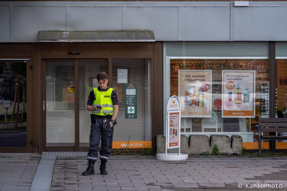 A security guard standing and looking at his phone outside a pharmacy.