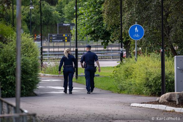 Two police officers walking down a path between som bushes.