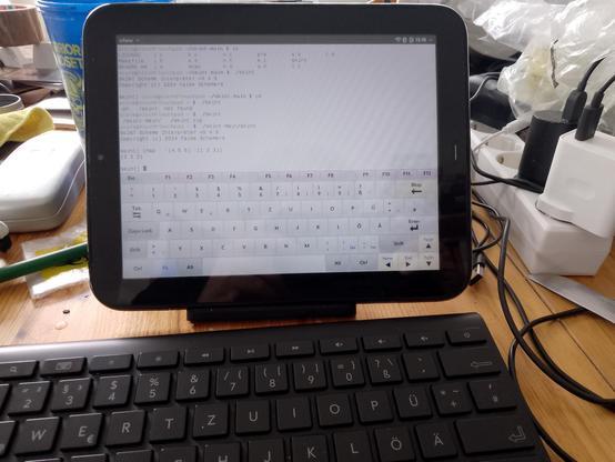 Photo of HP Touchpad on a rather untidy table. In the foreground is the HP wireless keyboard. The screen is showing the wterm terminal emulator running the skint scheme interpreter