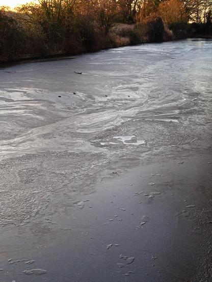 A crisp freezing dawn. A low sun of cold bronze shines through a veil of trees and shrub branches like cast copper. In the foreground the canal stretches out. Its surface, glazed and opaque a dull metalic grey. The surface is pitted and fissured with great swirling patterns (like Van Gogh's 'Starry Night').