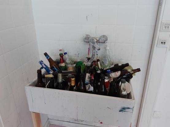 Blick auf ein Waschbecken vor gefliester Wand, drin sind ne Menge Bierflaschen