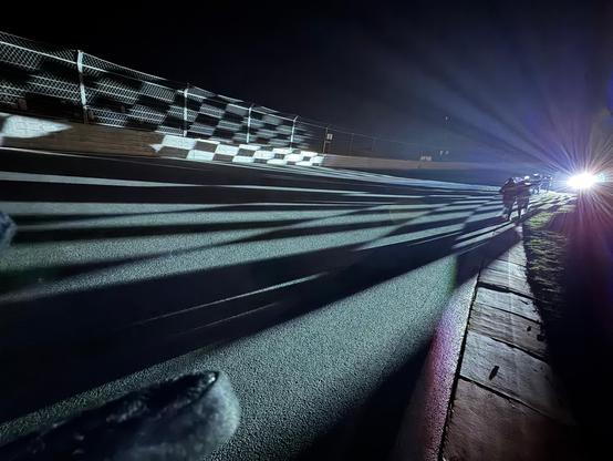 Foto gemaakt tijdens Zandvoort Light Walk 2025 op het circuit van Zandvoort in het donker met een projectie van een finishvlag op de rijbaan. Op de achtergrond lopen nog wandelaars.