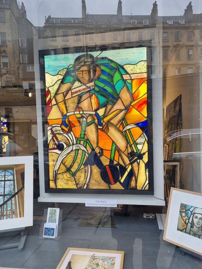 Framed artwork in stained glass of a male road cyclist, featured in the front window of a shop