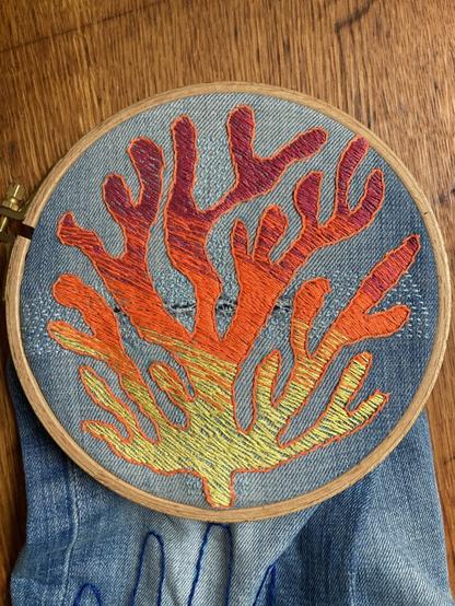A visible mending on the knee of a levi's jeans. The embroidery represents a coral with shades of yellow, orange and red threads.
