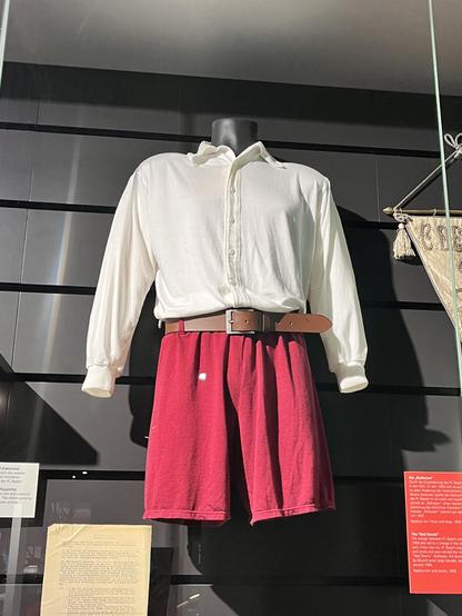 Hier sieht man das Rothosen-Outfit im Original. Das Oberteil hat eine durchgehende Knopfleiste. Die Hose wird durch einen breiten Ledergürtel gehalten.