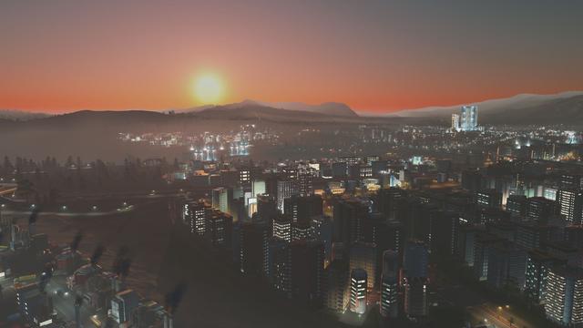 The sun sets behind some distant hills as the city below transforms into a sea of lights.