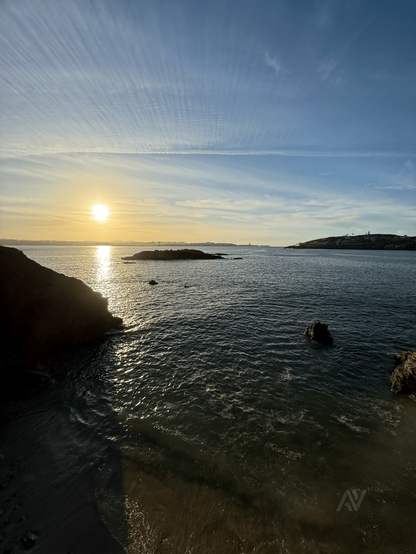 El la foto de puede ver el sol cayendo sobre la ciudad de Coruña desde la localidad de Mera. El cielo despejado solo con unas pocas nubes. El mar tranquilo.