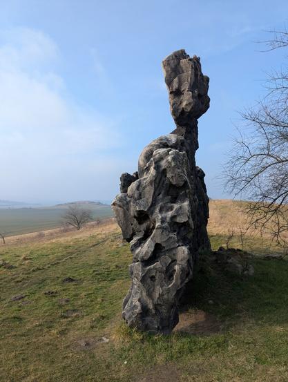 Close-up of a craggy, textured rock pillar against a backdrop of rolling hills and a clear sky, showing details of its unique shape and rough surface.