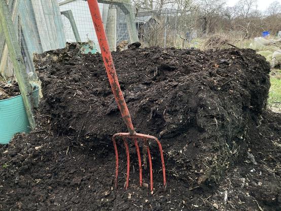 A pile of mature compost with a red pitchfork in front.