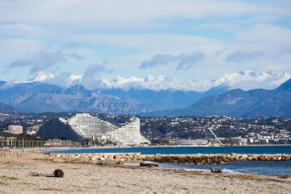 vorne unscharf Festungsmauer, dann Meer, dann Architektur, dann Berge und schneebedeckte Alpen
