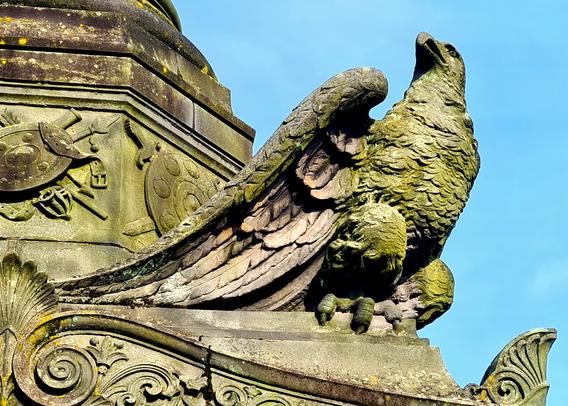 An eagle perched on the corner of a momunent with its wings swept backwards.