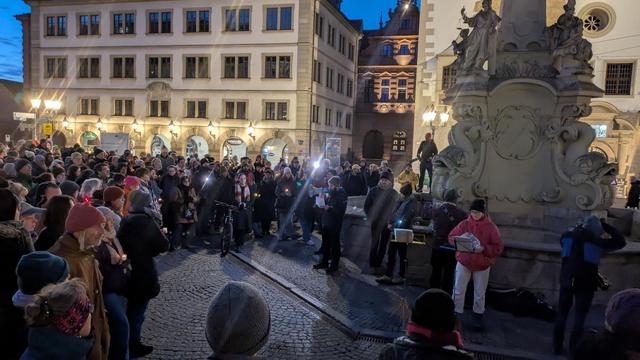 Die Menschenmenge mit Lichtern steht um den Vierröhrenbrunnen herum, vor dem gerade ein Redebeitrag vorgetragen wird.
