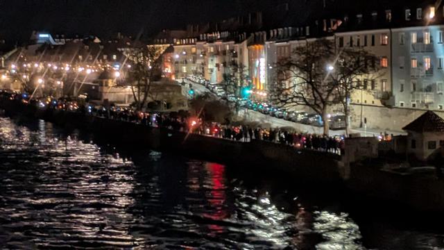 Von der Alten Mainbrücke aus fotografiert sieht man hunderte Menschen mit Taschenlampen, Kerzen und Handys den Mainkai in Richtung Friedensbrücke entlang laufen.
